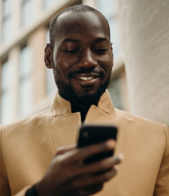 smiling man looking at his phone leaning on concrete pillar